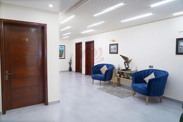 A spacious lobby with a wooden door labeled "102", a blue armchair, a small table with decorative items, and a framed picture on the wall. - Hotel Elegant Executive Suites (Multan)