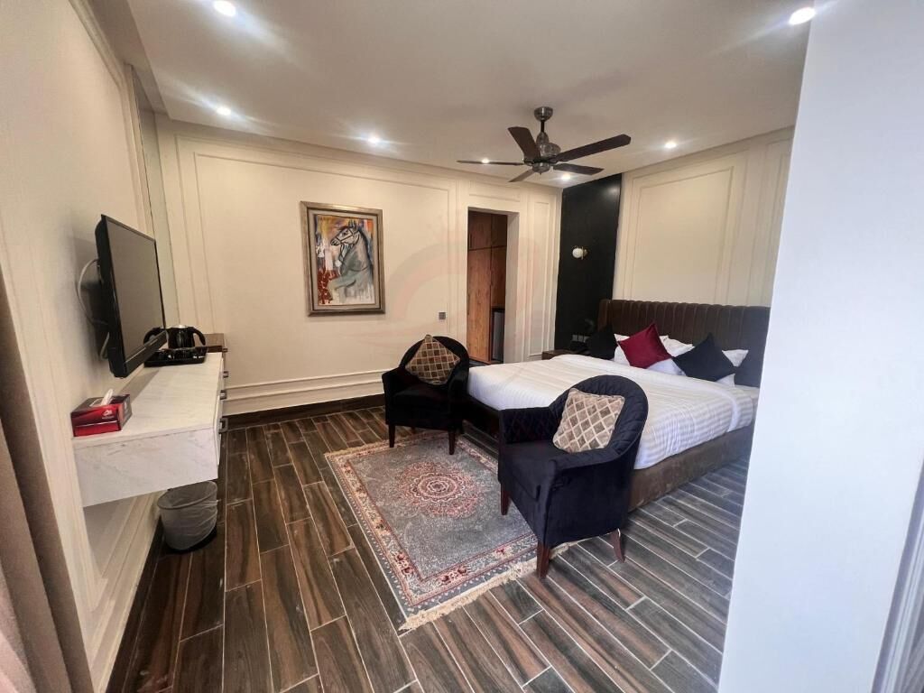 Un dormitorio con cama, escritorio, silla, televisión, ventilador de techo y un cuadro en la pared.