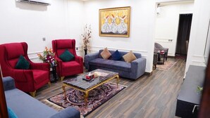 A living room with red and grey sofas, a coffee table, and a painting on the wall. - Hotel Elegant Executive Suites (Multan)