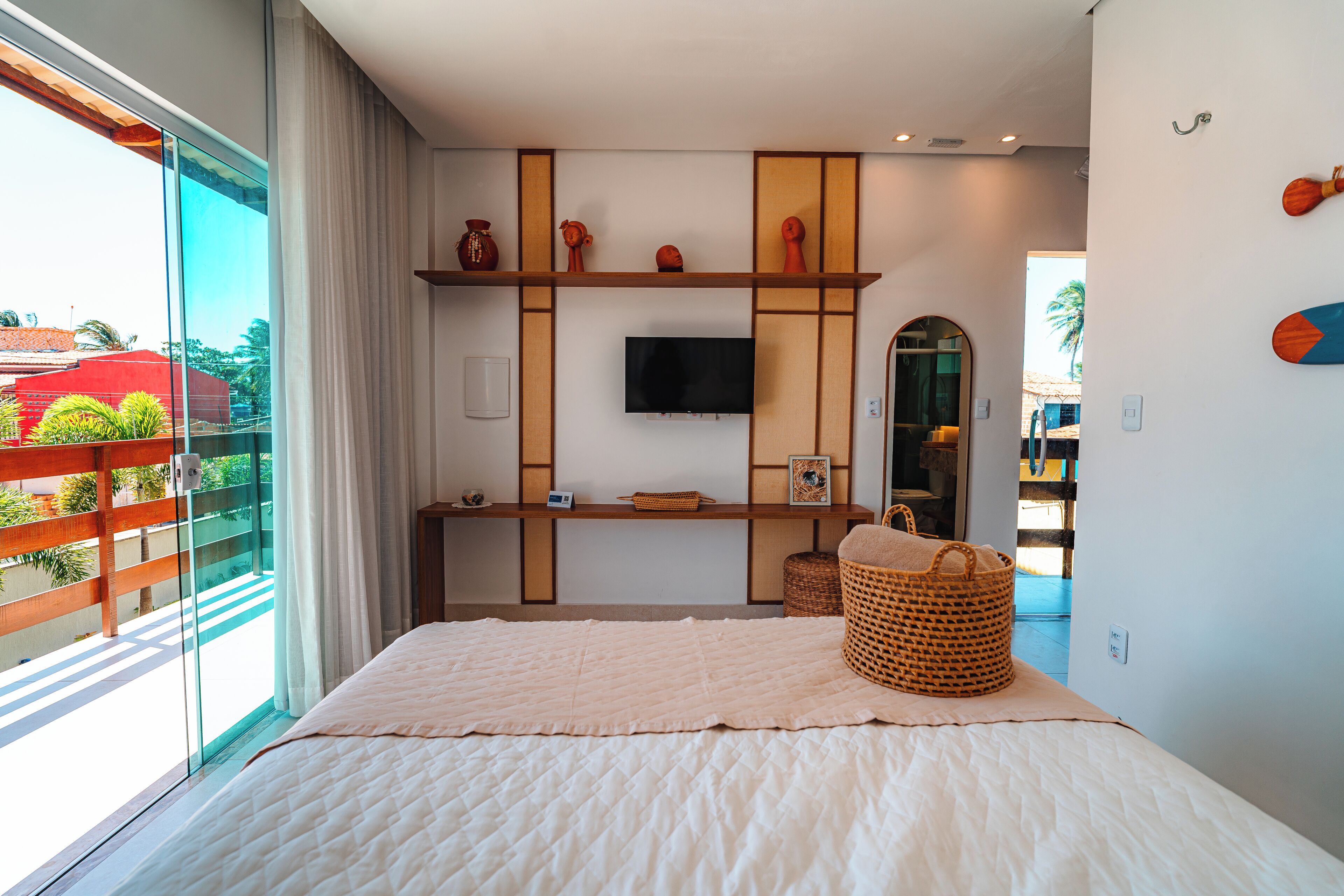 Un dormitorio moderno con una cama grande, un televisor montado en la pared y un balcón con vistas a palmeras.