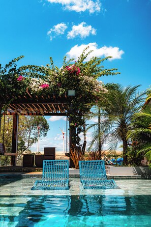 Ett poolområde med två blå stolar, en pergola med blommor och palmer.