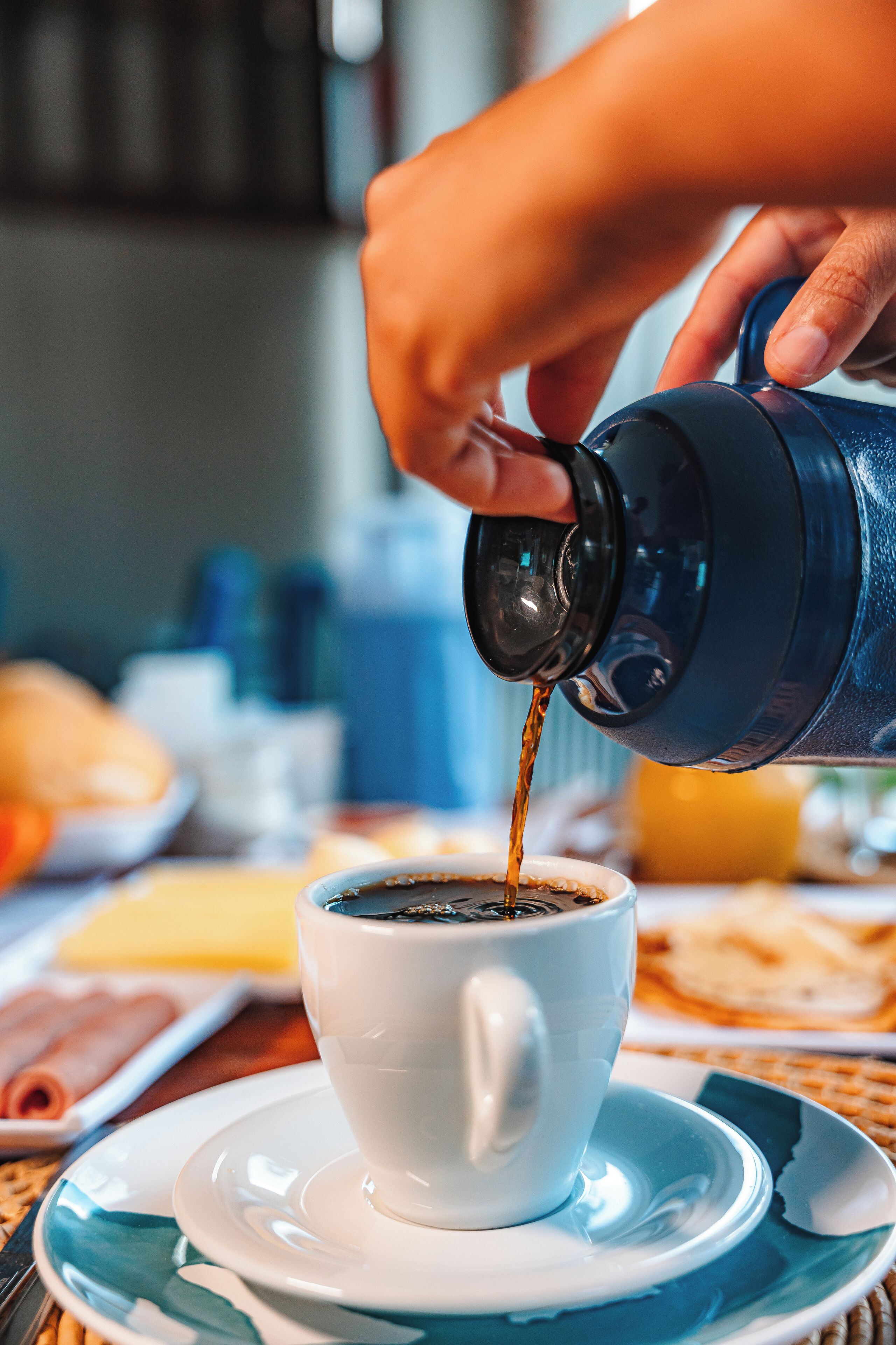 A hand pouring coffee into a white cup on a saucer.