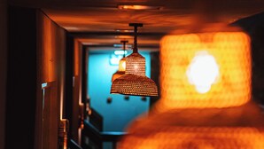 A hallway with a staircase leading to a room. A hanging lamp with a patterned shade is visible in the foreground. - POUSADA SOLLARI (Trairi)