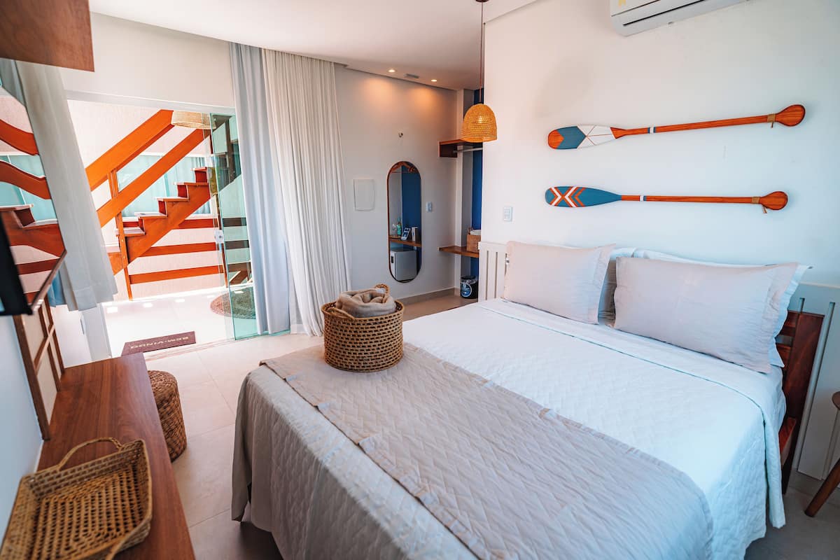 A hotel room with a large bed, a wooden bench, a wicker basket, and a view of a staircase.