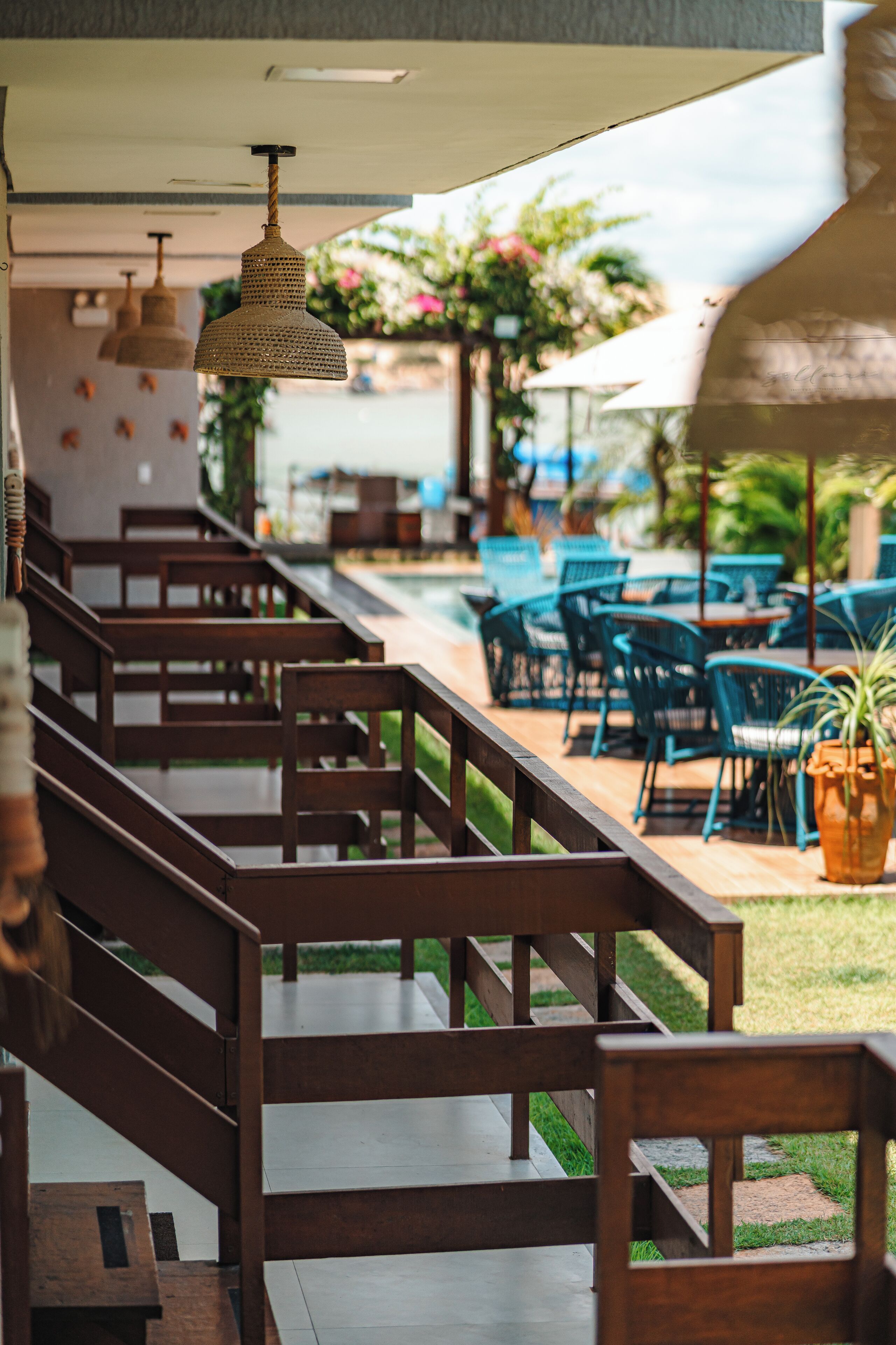 Un espace extérieur aménagé, abrité et doté de bancs et de tables en bois, entouré de verdure et de plantes en pot.