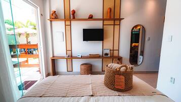A bedroom with a bed, a TV mounted on the wall, a wooden desk, and a large mirror.