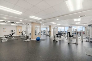 Ein Fitnessstudio mit verschiedenen Trainingsgeräten, einem blauen Übungsball und einem großen Fenster mit Tageslicht.