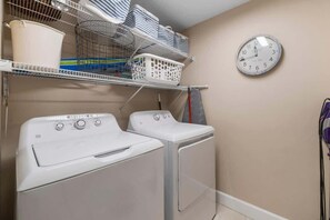 A laundry area with stacked laundry baskets, a white washing machine, and a wall clock.