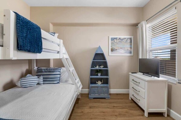 A bedroom with a bunk bed, a dresser, a TV, and a shelf with decorative items.