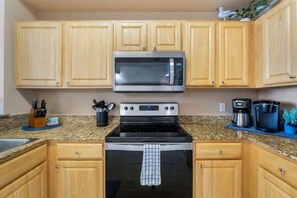 A kitchen with wooden cabinets, a stainless steel microwave, a stove, and a coffee maker.