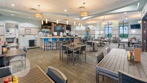 A spacious dining area with multiple tables and chairs, a kitchen area with bar seating, and large windows providing natural light.