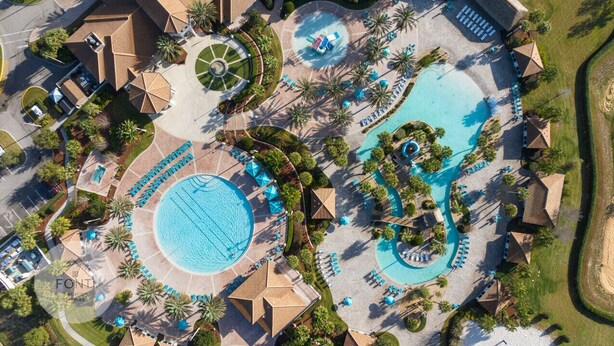 An aerial view of a resort with multiple swimming pools, sun loungers, and palm trees.