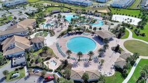 An aerial view of a resort with multiple swimming pools, palm trees, and a central circular pool.