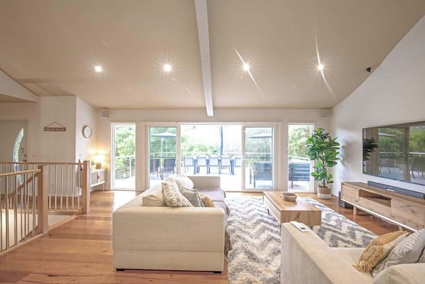 A spacious living room with a large sofa, a television, and a staircase leading to an upper floor.