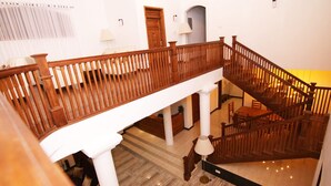 A multi-level wooden staircase with a railing, white walls, and a lamp on the lower landing. - Adaviya Resort (Mahiyanganaya)