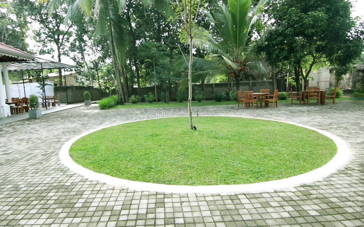 A circular grassy area with a paved walkway, surrounded by trees and outdoor furniture.