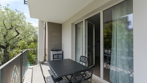 Un balcon avec une table et des chaises, une porte-fenêtre coulissante et une vue sur des arbres et un immeuble.