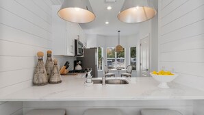 A modern kitchen with white cabinetry, a marble countertop, two pendant lights, a sink, and a bowl of fruit. - Seagrove "30Astrella Del Mar" |4BR |Private Pool|3min walk to beach access! (Santa Rosa Beach)