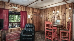 A wooden cabin interior with a leather chair, a red wooden table, and a television. - Lofty Pines Cabin (Ruidoso)