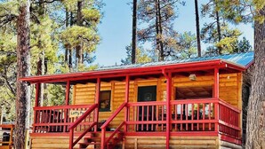 A wooden cabin with a red exterior, a porch with red railings, and a staircase leading to the entrance. - Lofty Pines Cabin (Ruidoso)