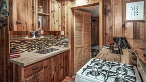 A rustic kitchen with wooden cabinets, a tiled backsplash, and a gas stove. - Lofty Pines Cabin (Ruidoso)