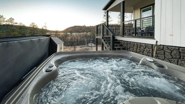 A hot tub with a view of a house and surrounding landscape.
