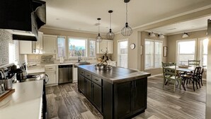 A modern kitchen with a central island, pendant lighting, and a dining area with chairs.