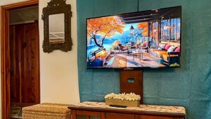 Uma televisão presa a uma parede azul-turquesa, um armário de madeira com gavetas e um banquinho de vime.