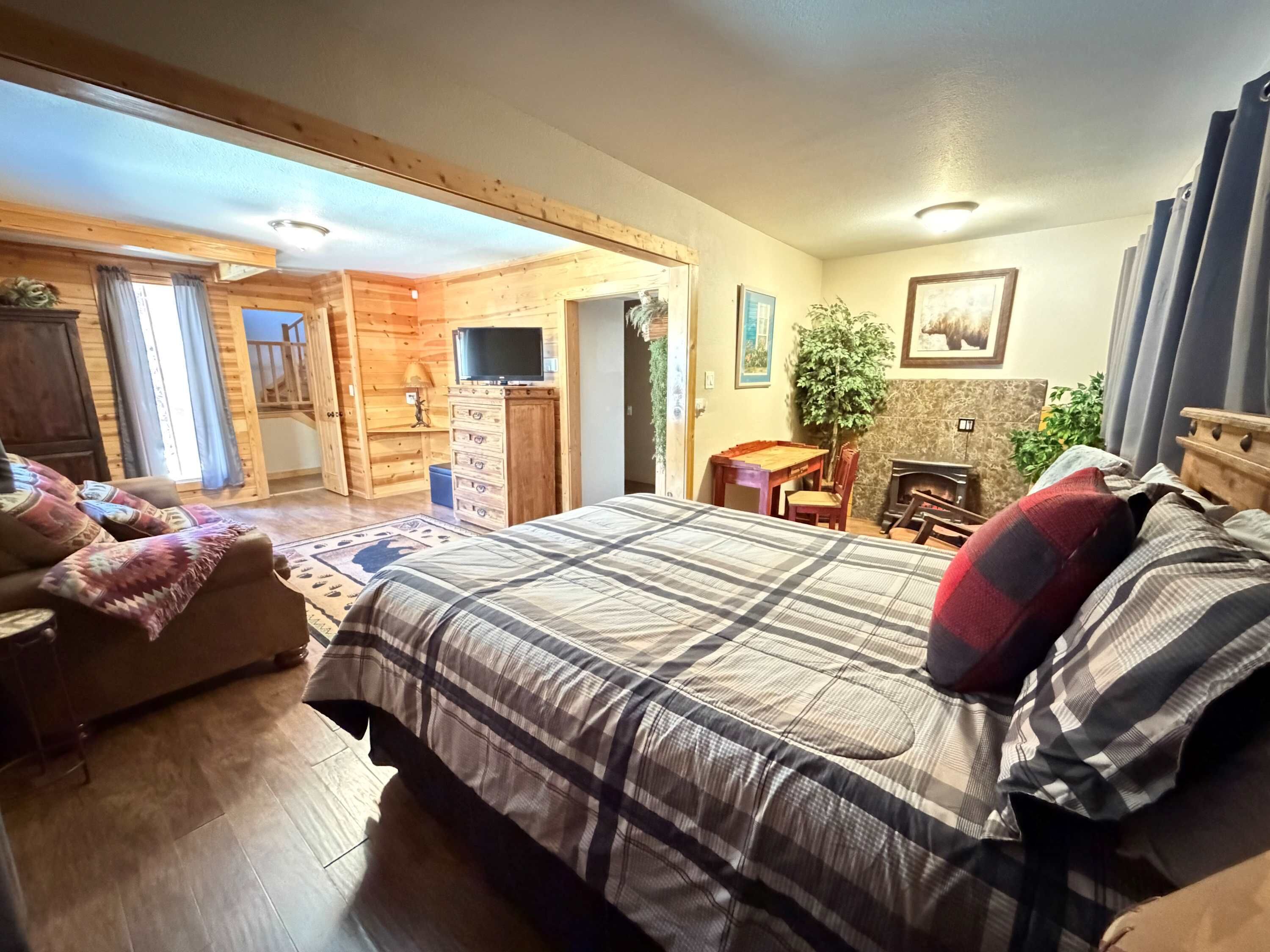 A cozy room with a large bed, a wooden dresser, a television, and a dining area with a table and chairs.