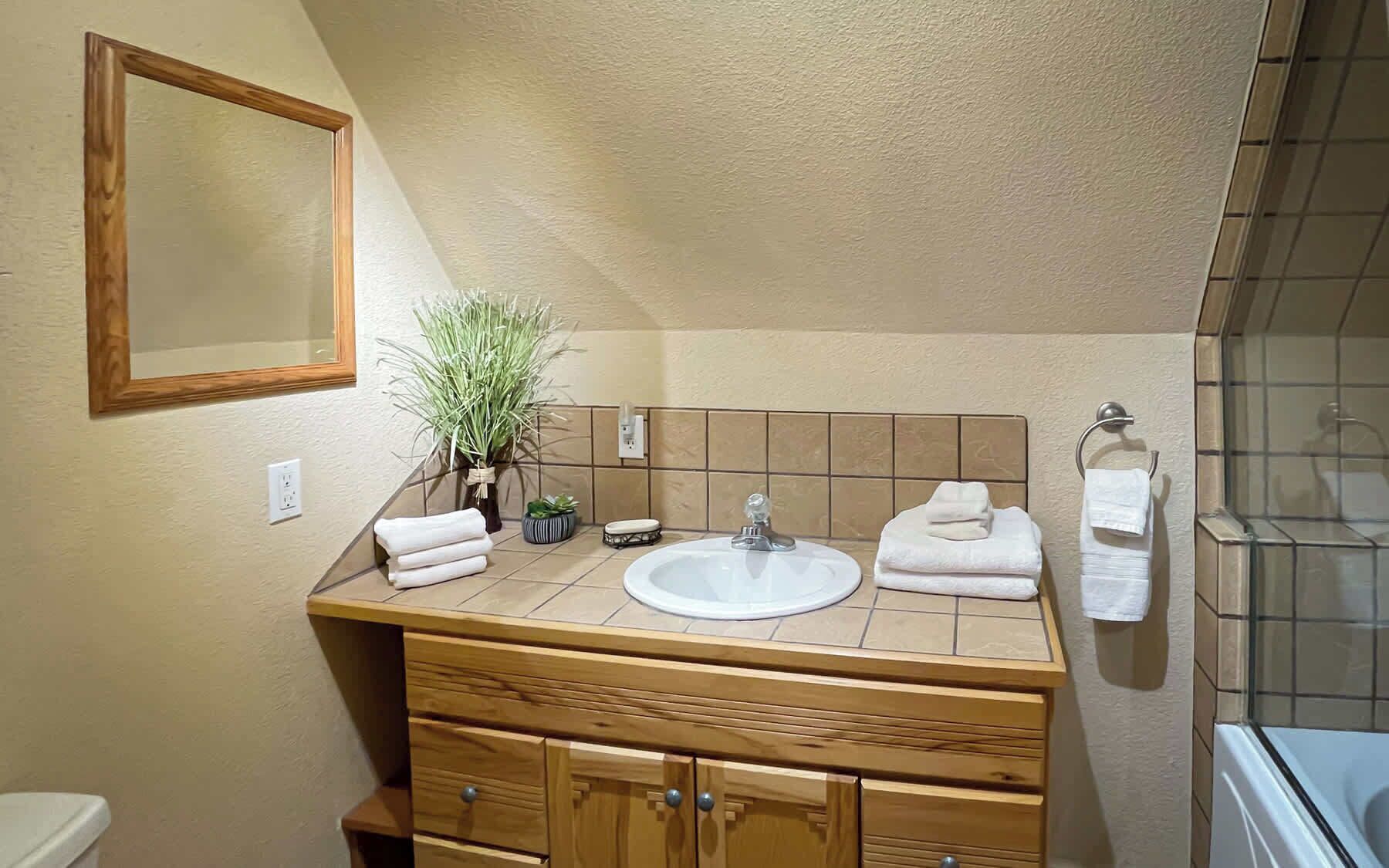 A bathroom with a wooden vanity, a sink, a mirror, and a shower area.