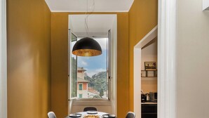 Un comedor con una mesa dispuesta para seis personas, una lámpara colgante negra y vistas a una colina a través de una ventana.