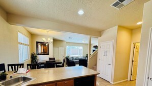 A kitchen with a granite countertop, wooden cabinets, a dishwasher, and a dining area with a table and chairs. - Palm Paradise by Mesquite Vacation Rentals with Community Pool, Two Primary Suites and $510 in free daily activities (Mesquite)
