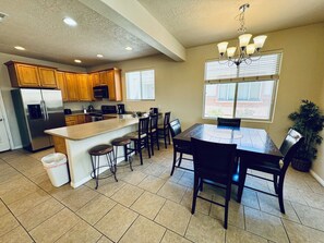 A kitchen with a central island, bar stools, a dining table with chairs, a refrigerator, and a chandelier.