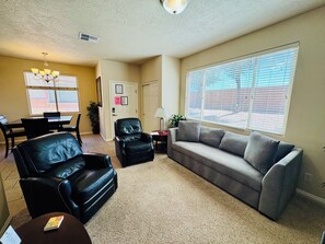 A living room with a sofa, chairs, a dining table, and a large window with blinds.