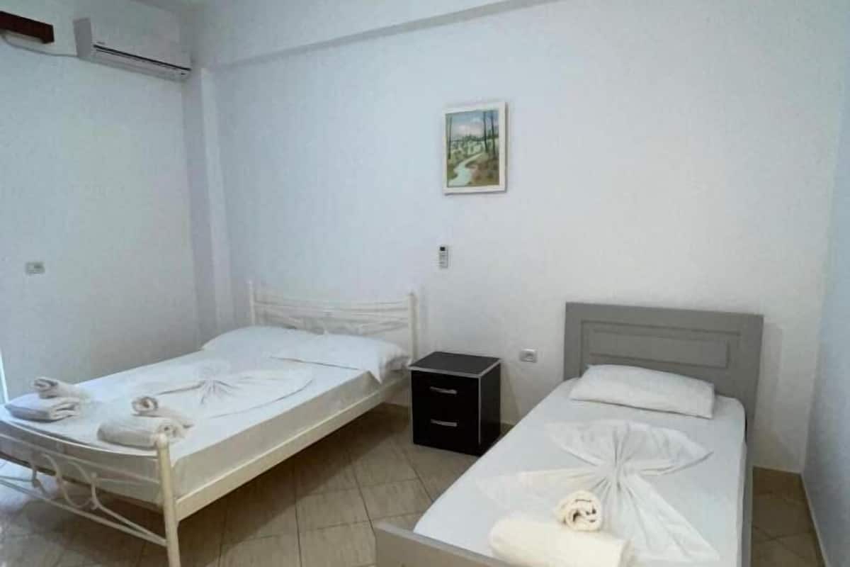 Una habitación con dos camas individuales, una mesita de noche pequeña, aire acondicionado instalado en la pared y un cuadro en la pared.