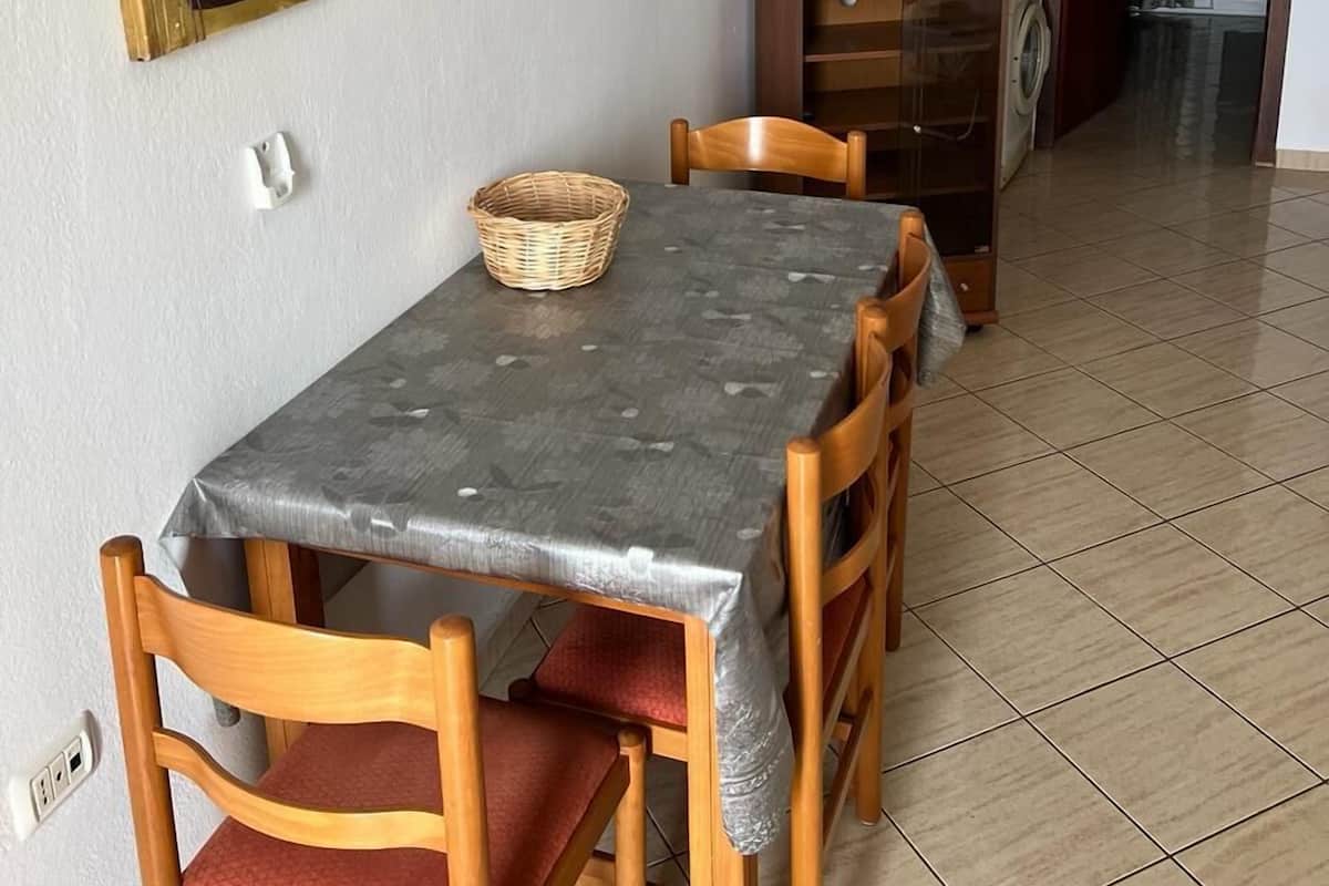 Un comedor con una mesa, sillas, un televisor sobre un soporte, un cuadro en la pared y un pasillo que conduce a otra habitación.