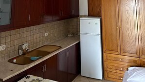 A compact kitchen with dark wooden cabinets, a white refrigerator, and a tiled backsplash. - Villa AlMar (Sarandë)