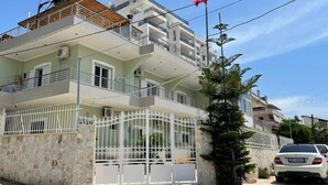 A multi-story residential building with balconies, a gated entrance, and a flag. - Villa AlMar (Sarandë)