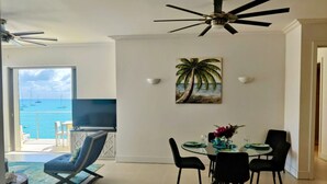 Un comedor con vista al mar, un ventilador de techo y un cuadro de una palmera.