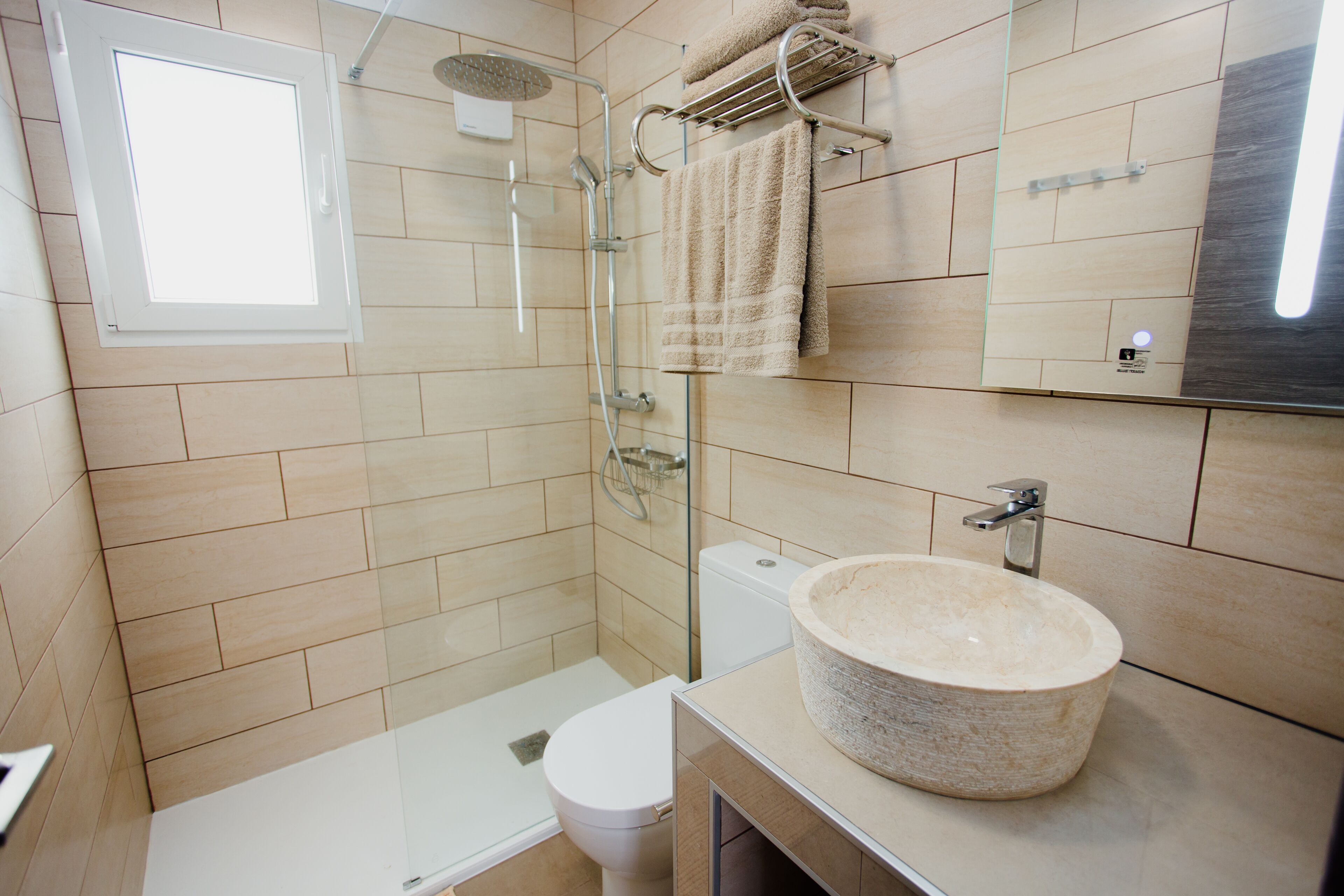 Un baño moderno con ducha envuelta en vidrio, inodoro blanco y un lavamanos de piedra grande.