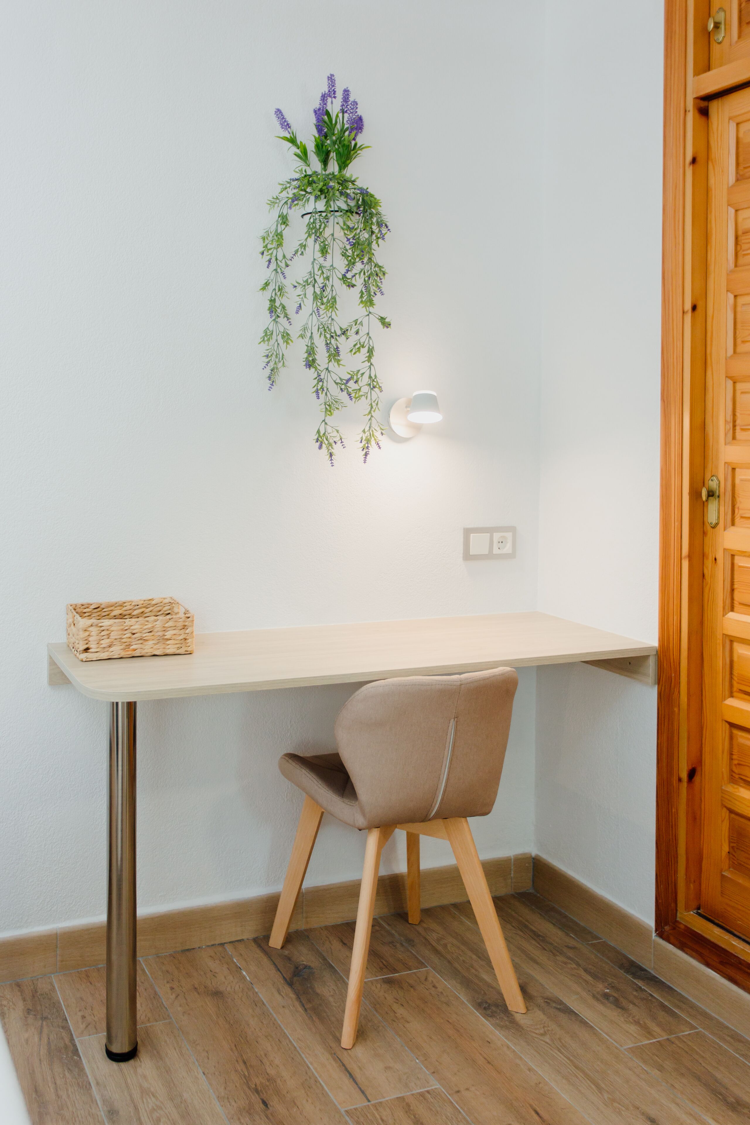 Un bureau d’angle avec une chaise, une plante suspendue et un luminaire fixé au mur.