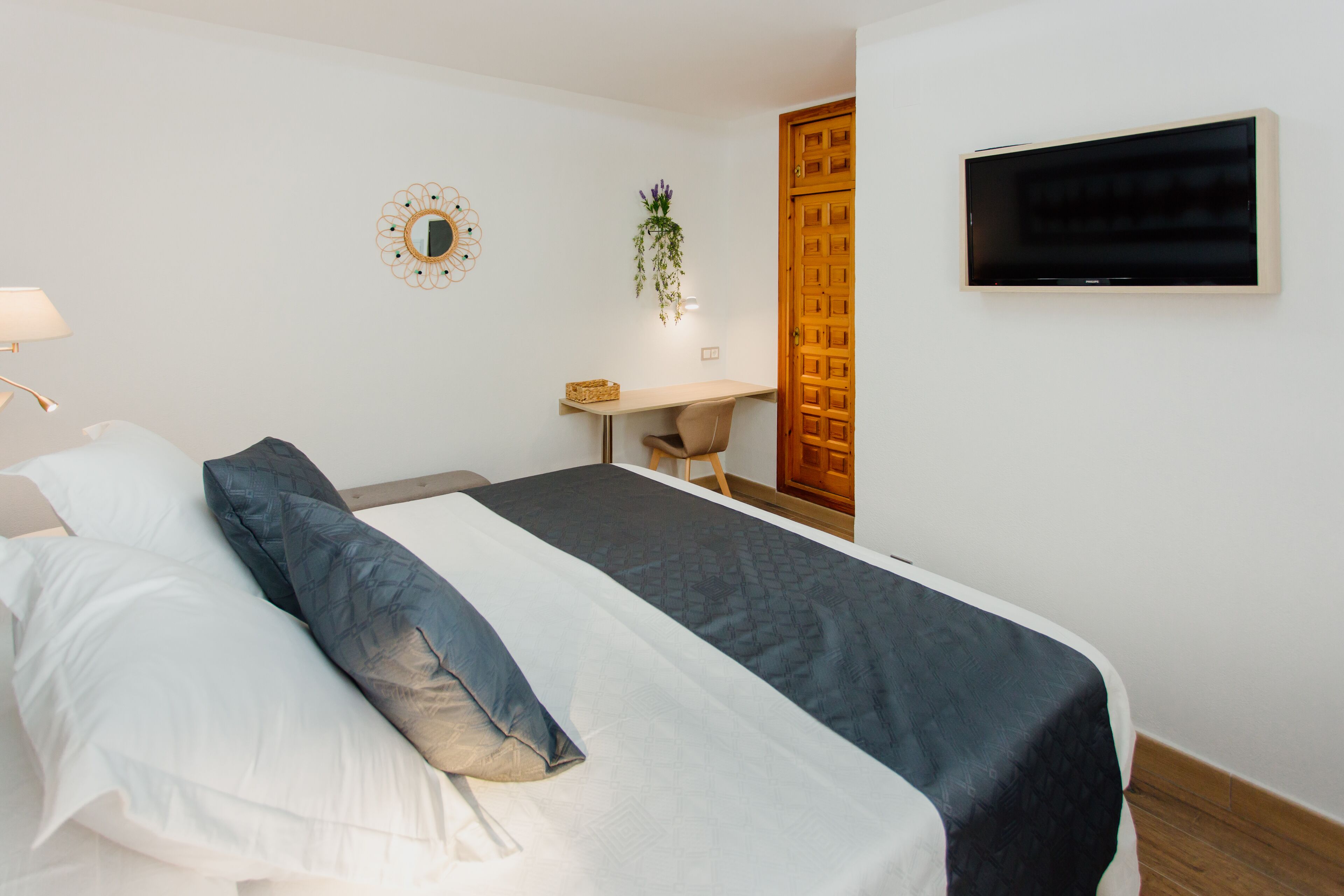 Een slaapkamer met een bed, een bureau, een stoel, een televisie en een deur.