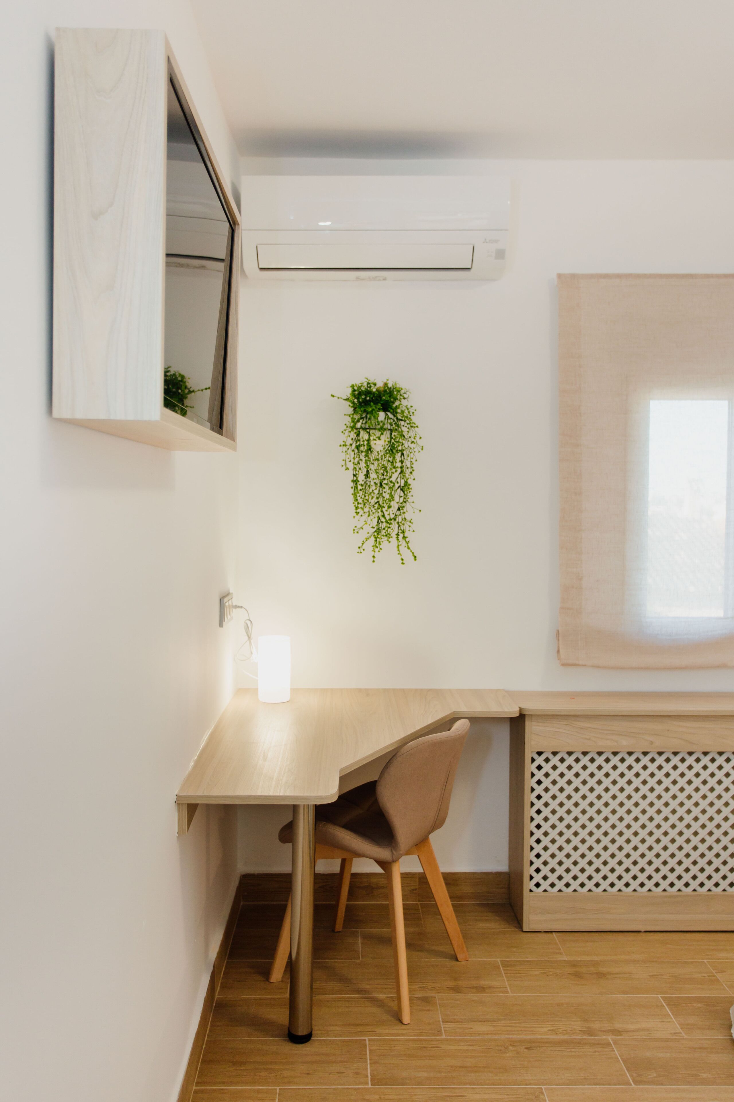 Une chambre moderne avec un bureau en bois, une chaise, une plante suspendue et une fenêtre donnant sur un beau paysage.