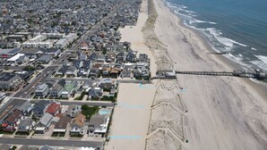 Luftaufnahme einer Küstenstadt mit einem langen Strand, einer Mole und dicht bebauten Wohngebieten.
