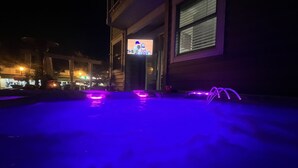Ein Whirlpoolbereich mit einem Fernseher, der ein Sportevent zeigt, umgeben von einem Gebäude mit einem Fenster und einer Tür.