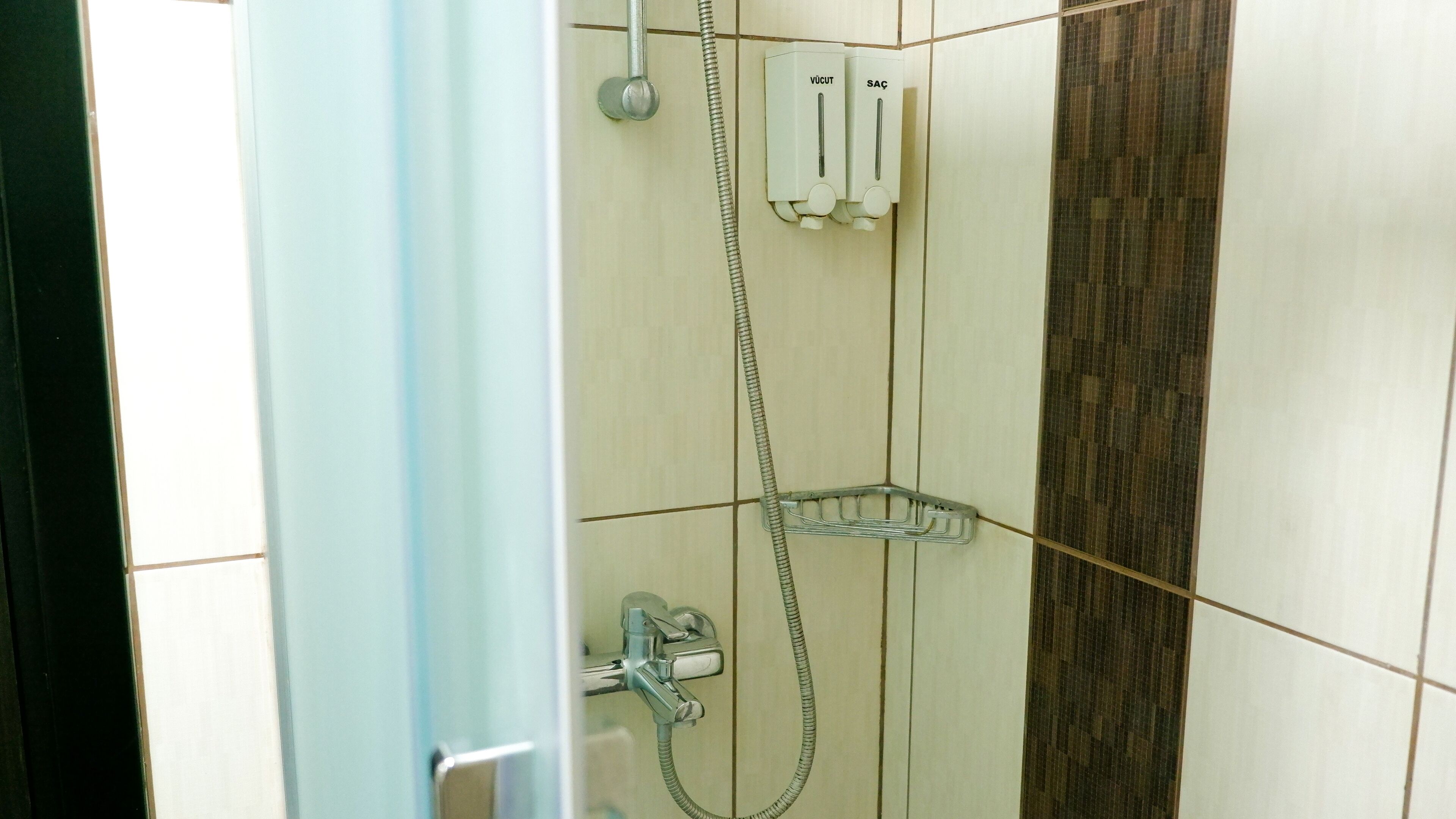 Un área de ducha con cabezal de ducha manual, llave de pared y panel de control.