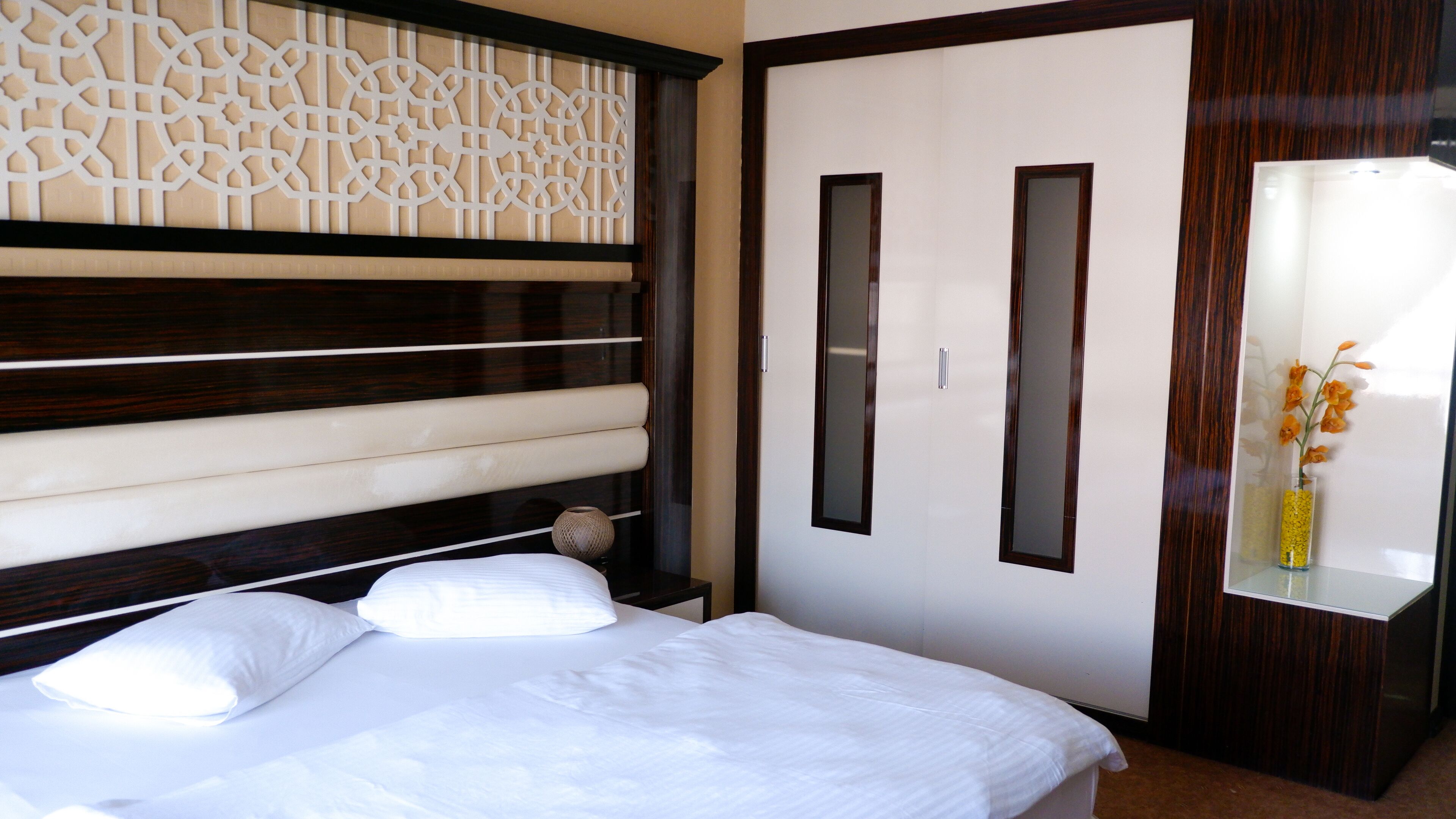 A neatly made bed with white linens, a wooden headboard, and a decorative wall panel.