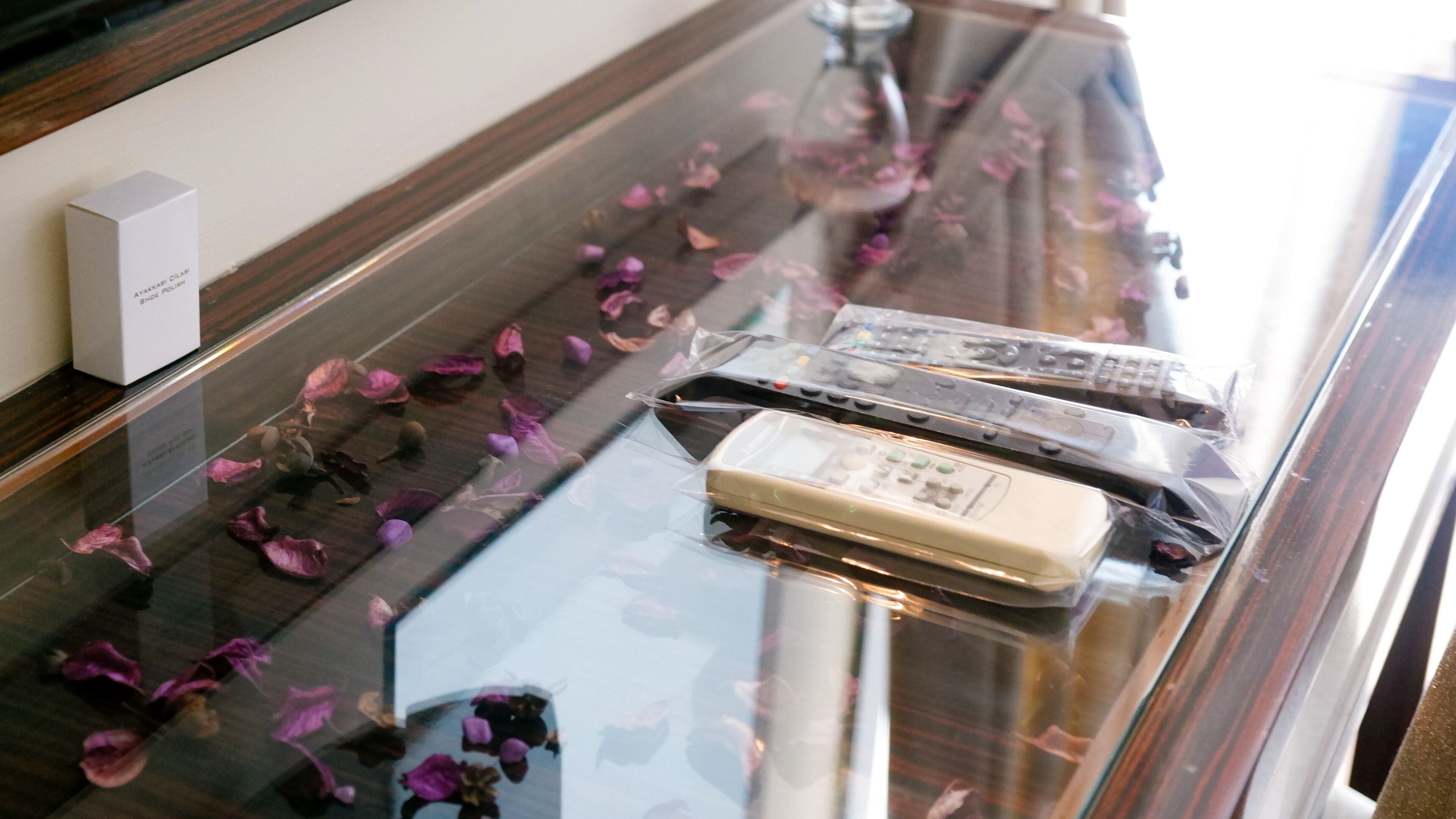 A glass-topped table with rose petals, a white box, and several electronic devices in plastic packaging.