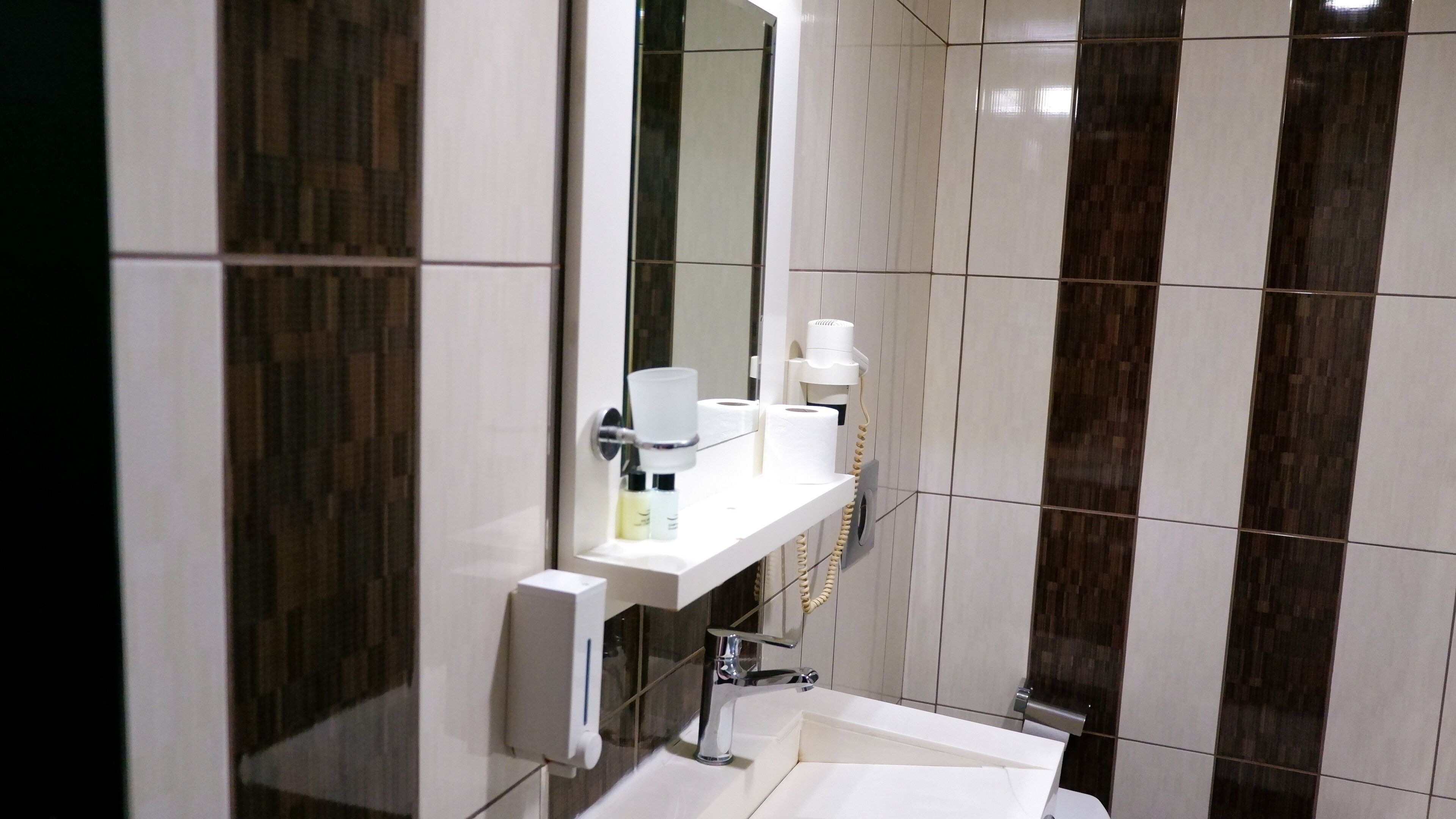A modern bathroom with a white sink, mirror, and dark patterned tiles.