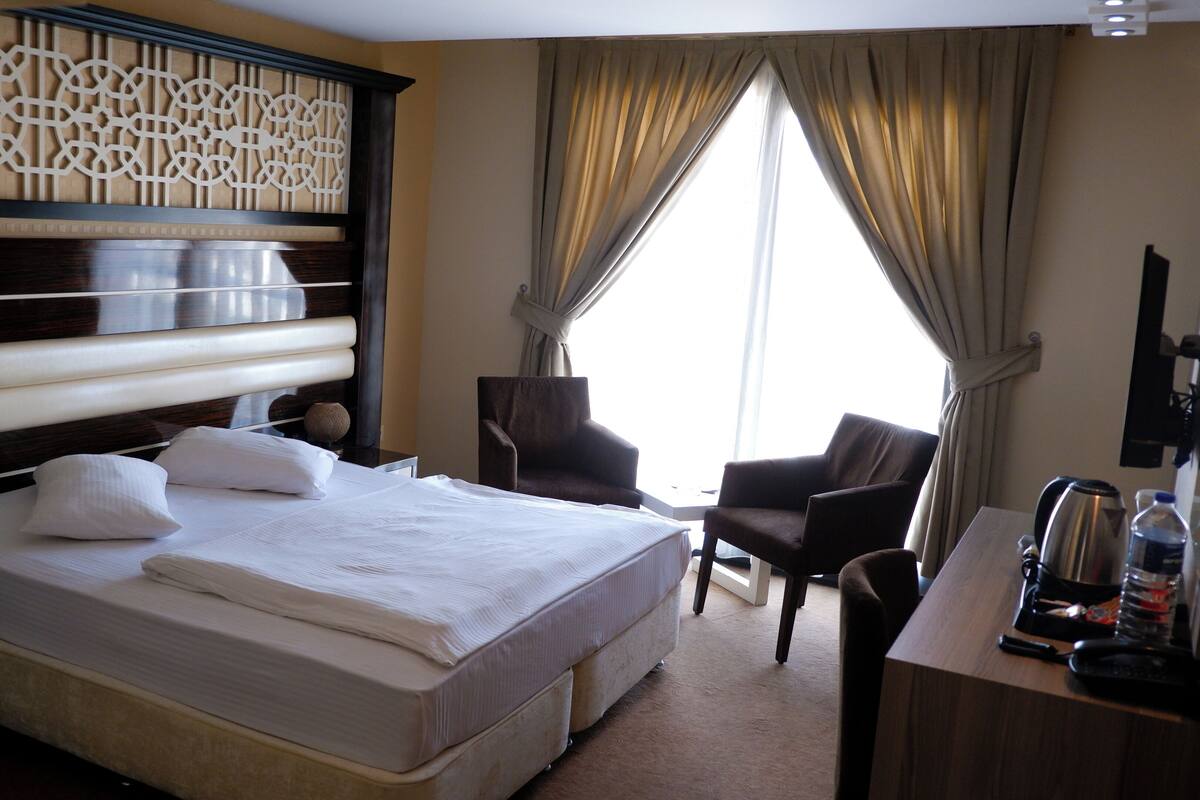 Ein Hotelzimmer mit einem großen Bett, einem Schreibtisch mit Wasserkocher und einem Sessel.
